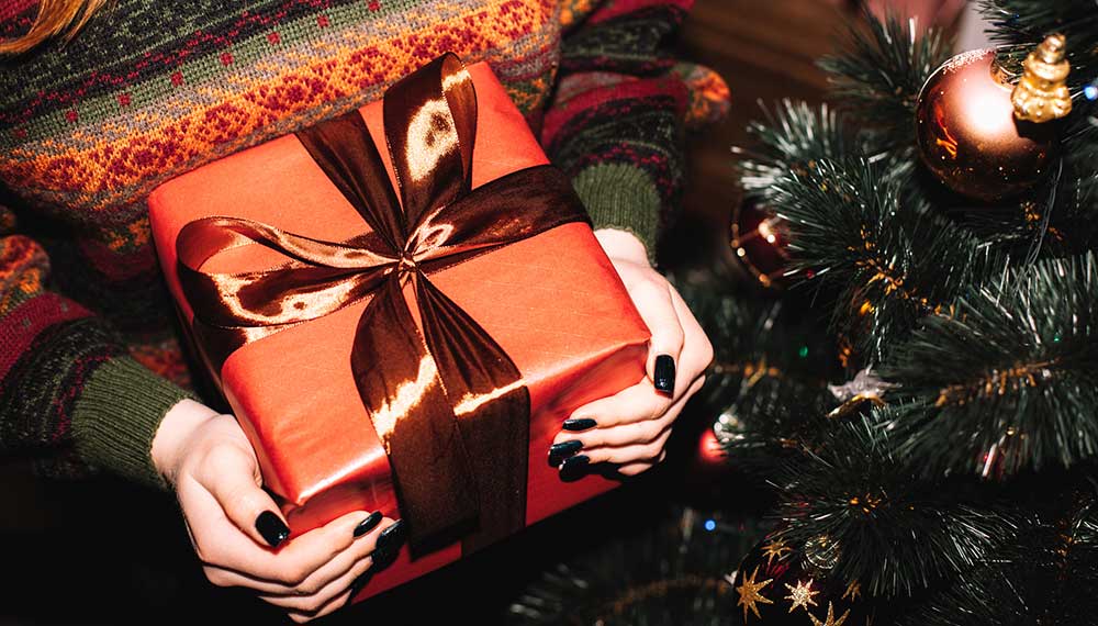Close up of woman holding a red-wrapped gift next to a Christmas tree
