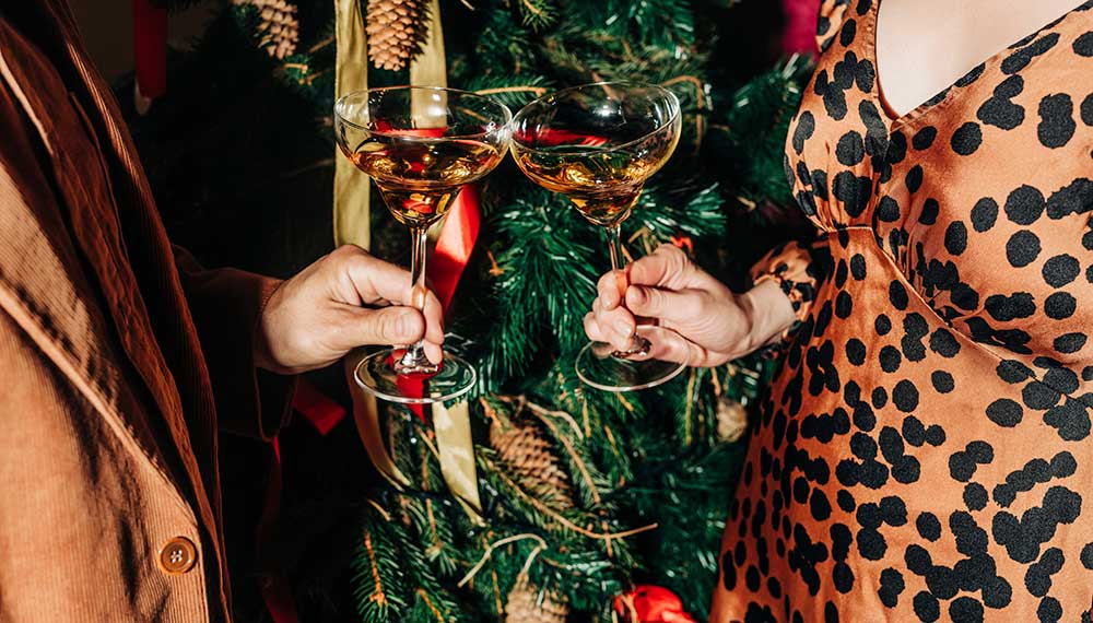 Close up of two people standing in front of a Christmas tree, clinking glasses