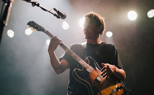 man holding guitar on stage with microphone